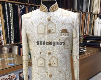 Könnte beinhalten: Ein weißes, langärmeliges Kleidungsstück mit einem Stehkragen und goldenen Stickereien. Das Kleidungsstück hat einen Knopfleisten vorne und eine Tasche auf der linken Seite. Das Kleidungsstück ist mit einem Muster aus goldenen Quadraten und floralen Motiven verziert. Der Text "URdesigners" ist auf dem Kleidungsstück sichtbar.