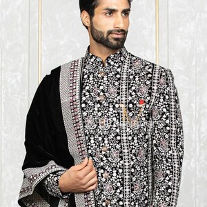 May include: A black velvet shawl with a silver and pink embroidered border. The shawl is draped over a man wearing a black embroidered jacket with a white floral pattern.