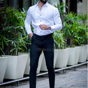 May include: A white dress shirt with a pleated front and black buttons, paired with black trousers and black boots. The image also shows a watch and sunglasses. The text "URdesigners" is visible.