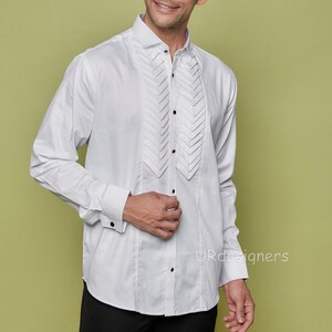 May include: A white long-sleeve dress shirt with a pleated front and black buttons. The shirt has a classic collar and French cuffs.