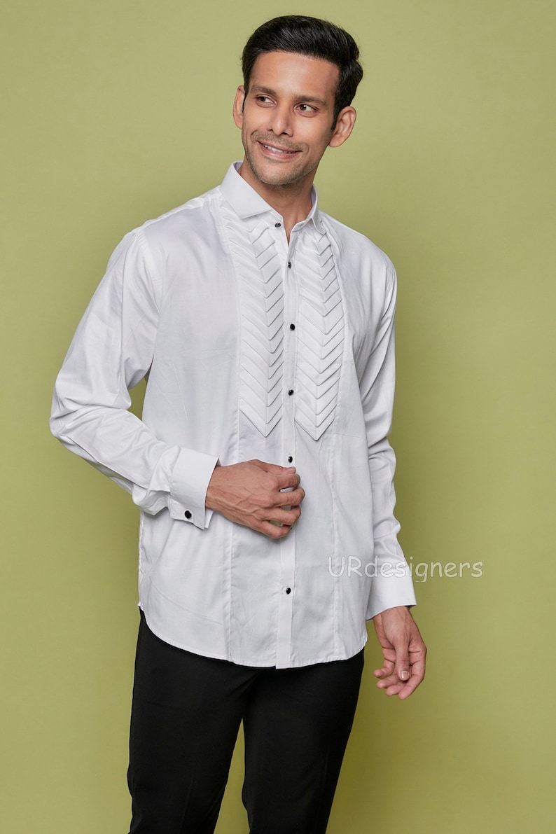 May include: A white long-sleeve dress shirt with a pleated front and black buttons. The shirt has a classic collar and French cuffs.