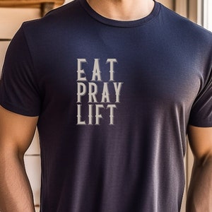 Puede incluir: Una camiseta azul marino con el texto "EAT PRAY LIFT" impreso en blanco en la parte delantera.