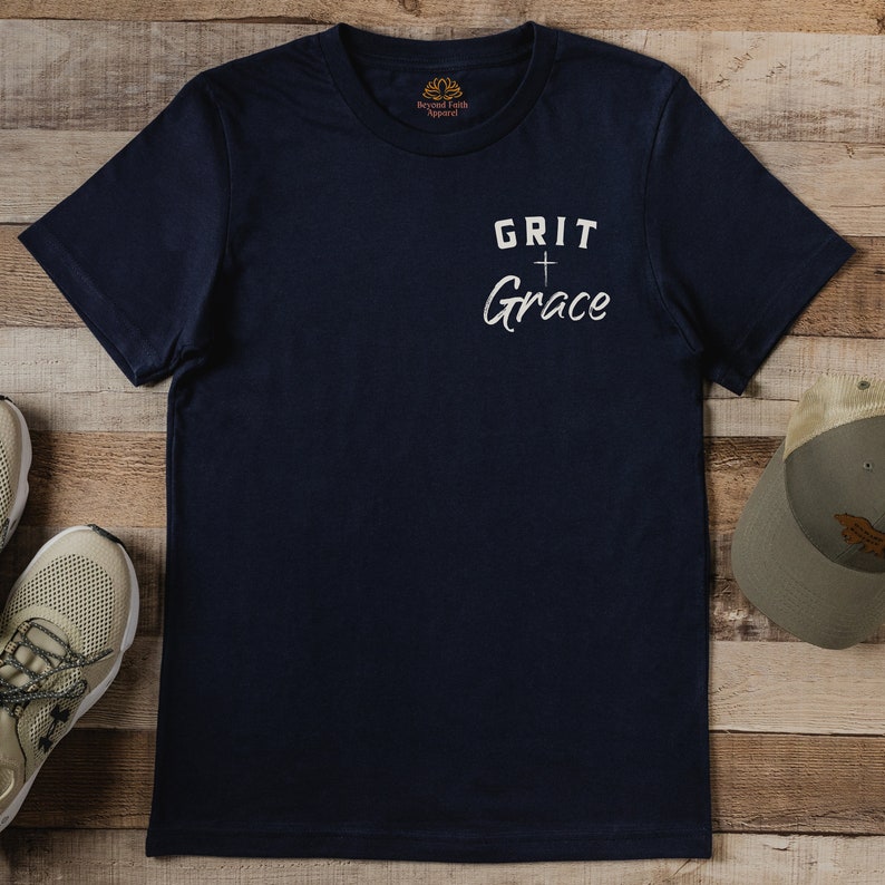 Op de afbeelding: Een marineblauw t-shirt met een witte afbeelding met de tekst "GRIT + Grace".