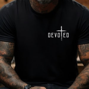 以下が含まれることがあります： 白い十字架と「DEVOTED」という文字が前面にプリントされた黒いTシャツ