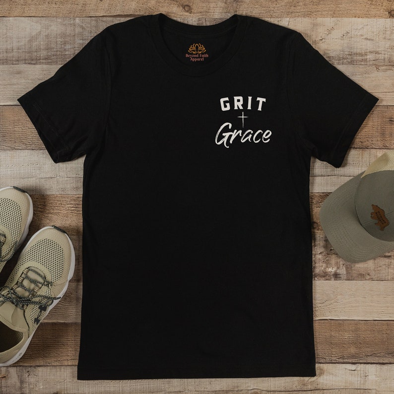 Op de afbeelding: Zwart T-shirt met witte tekst die "GRIT + Grace" luidt.
