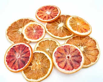 May include: A collection of dried orange slices, some with a red hue, arranged on a white surface. The slices are various sizes and shapes, with some showing the seeds inside.
