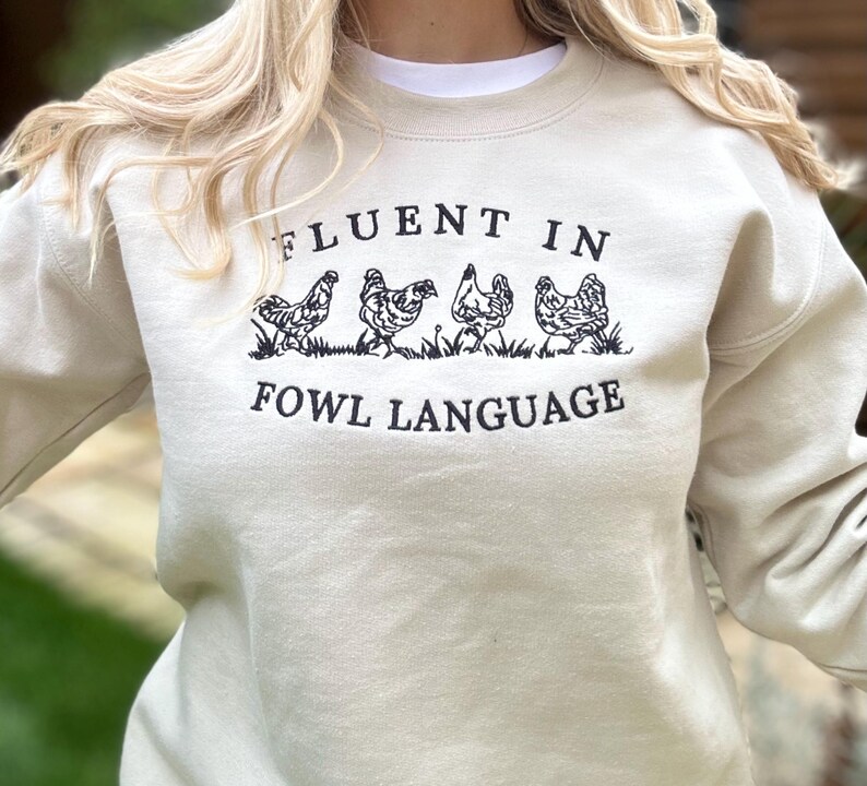 May include: A light beige sweatshirt with the text "Fluent in Fowl Language" and a graphic of four chickens walking in a line.
