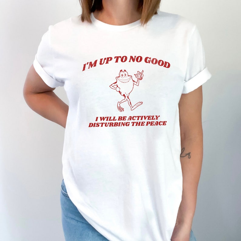 May include: White t-shirt with red text that reads "I'm up to no good" and a cartoon frog. The text below the frog reads "I will be actively disturbing the peace."
