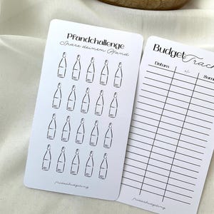 May include: Two white cards with black text and illustrations. One card has a bottle illustration and the text "Pfandchallenge Spare deinen Pfand". The other card has a budget tracker with the text "Budget Tracker".