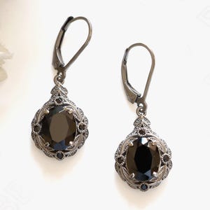 May include: A pair of antique-style earrings with a dark gunmetal finish. Each earring features a large, oval-cut black gemstone surrounded by a detailed filigree design. The lever-back closures add a classic touch to these elegant earrings.