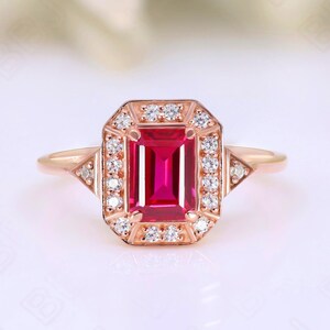 Puede incluir: Un anillo de oro rosa con un gran rubí de talla esmeralda rodeado por un halo de diamantes más pequeños.