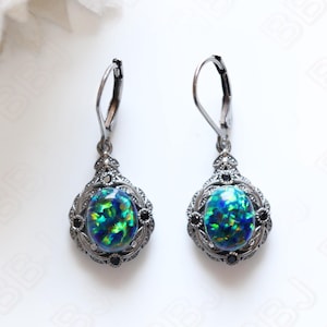 May include: A pair of silver dangle earrings with a green and blue opal stone set in a silver filigree design. The earrings have black accents and a lever back closure.
