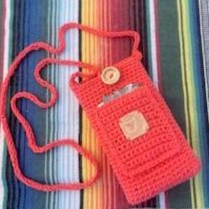 May include: A bright coral crocheted crossbody bag with a long strap and a wooden button closure. The bag has a small pocket on the front.
