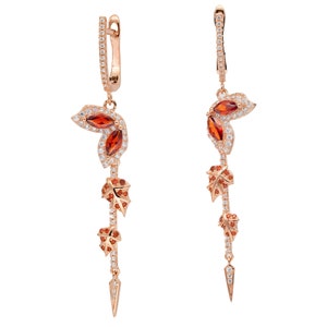 May include: Rose gold dangle earrings with a leaf design featuring clear and orange gemstones.