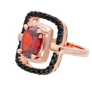 May include: A rose gold ring with a large red gemstone surrounded by a black stone halo.