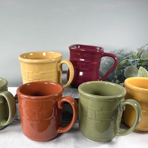 May include: A collection of six ceramic mugs featuring a raised basket-weave texture on the exterior. The mugs are finished in various solid colors including olive green, mustard yellow, burnt orange, and a deep burgundy red.