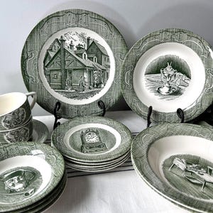 May include: A collection of green and white vintage dinnerware. The set includes plates, bowls, and teacups with detailed illustrations of buildings, clocks, and other scenes. The plates have a decorative border.