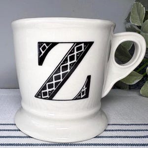Pu&ograve; includere: Tazza in ceramica bianca con un design a lettera "Z" nera. La lettera &egrave; riempita con un motivo a diamante. La tazza ha un manico unico e una base a piedistallo. Un oggetto decorativo per la cucina o la casa.