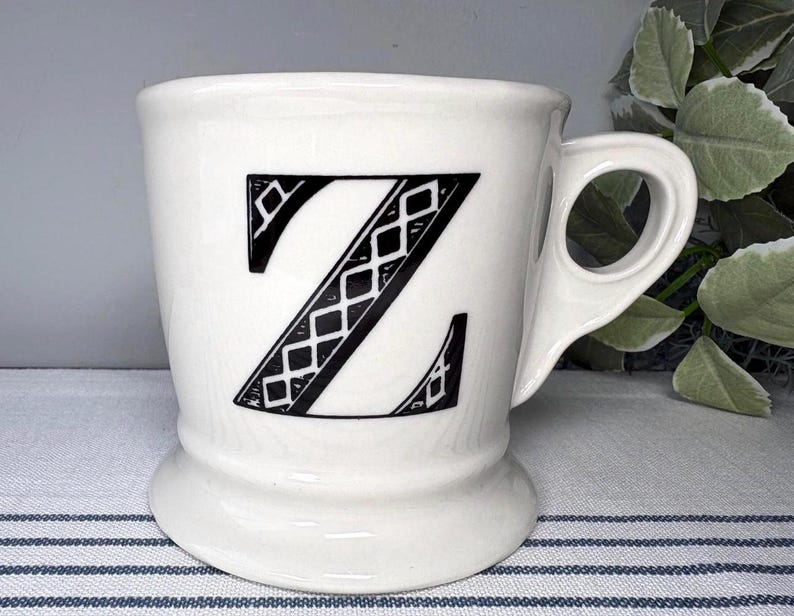 Pu&ograve; includere: Tazza in ceramica bianca con un design a lettera "Z" nera. La lettera &egrave; riempita con un motivo a diamante. La tazza ha un manico unico e una base a piedistallo. Un oggetto decorativo per la cucina o la casa.