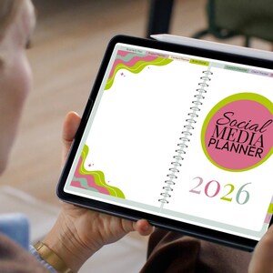 K&ouml;nnte beinhalten: Ein digitaler Planer f&uuml;r 2026 mit Spiralbindung. Der Planer zeigt auf dem Cover den Text "Social Media Planner" in einem rosa Kreis, mit gr&uuml;nen und rosa Wellenmustern. Ein Stift ist auf dem Ger&auml;t sichtbar.