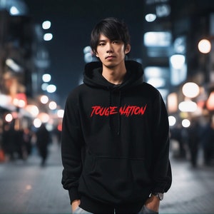 Puede incluir: Sudadera negra con el texto rojo "TOUGE NATION" en el pecho. La imagen est&aacute; tomada de noche en una calle de la ciudad con luces borrosas en el fondo. La sudadera tiene capucha y mangas largas.