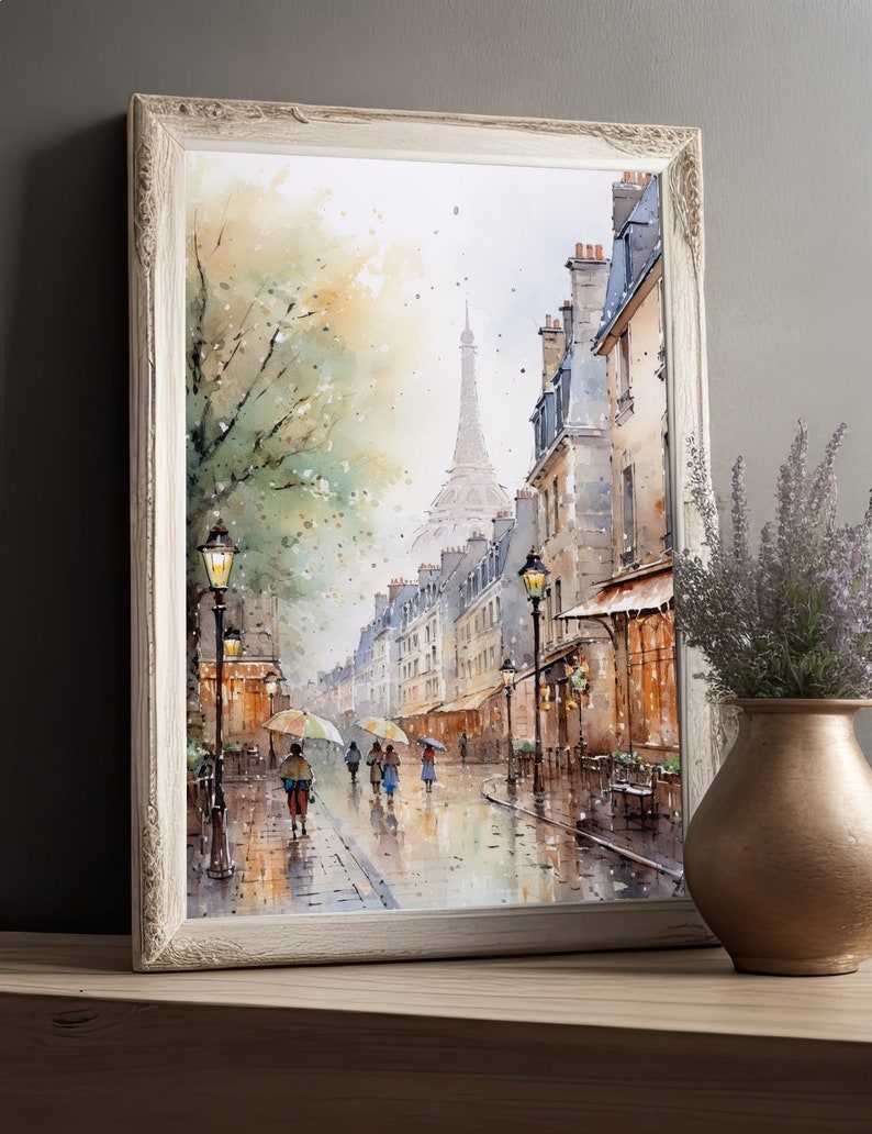May include: A watercolor painting of a Parisian street scene with a view of the Eiffel Tower in the distance. The street is lined with buildings and trees, and there are people walking with umbrellas. The painting is framed in a white frame.