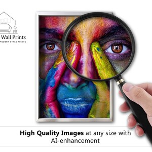May include: A close-up of a person's face with colorful paint on their skin. A magnifying glass is being used to highlight the detail of the paint. The image is framed in a white frame with a silver border. The text "Elegant Wall Prints" is at the top of the image.