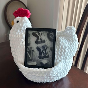 May include: White crocheted chicken-shaped book holder with a red comb and a black e-reader inside.