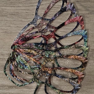 May include: A stack of colorful eyeglass frames with a unique, patterned design. The frames feature a mix of colors including blue, purple, green, and brown. The frames are arranged on a wooden surface.