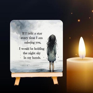May include: A square decorative tile on a small wooden easel featuring a watercolor illustration of a person standing in water under a cloudy sky. The text reads: If I held a star every time I am missing you, I would be holding the night sky in my hands.