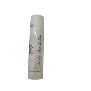 May include: A white lip balm tube with a white cap. The label features the text "Herbal Mint Lip Balm" in a script font, along with a floral design in pink and purple. The tube has a textured, wood-like appearance.