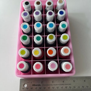 May include: A pink plastic container with 36 small bottles of liquid food coloring. The bottles are arranged in a 6x6 grid. The colors include red, orange, yellow, green, blue, purple, brown, and black.