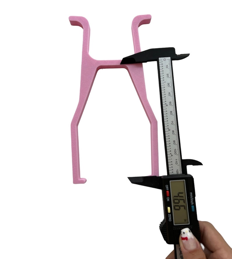 May include: Pink plastic H-shaped object being measured with a digital caliper. The caliper reads 466 mm.