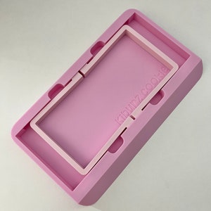 May include: A pink silicone mold with a raised rectangular frame inside. The mold has the text "klown2cookie" printed on the side.