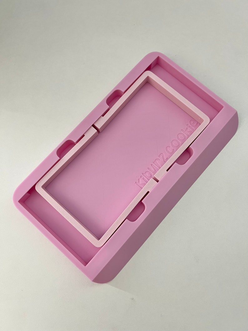May include: A pink silicone mold with a raised rectangular frame inside. The mold has the text "klown2cookie" printed on the side.