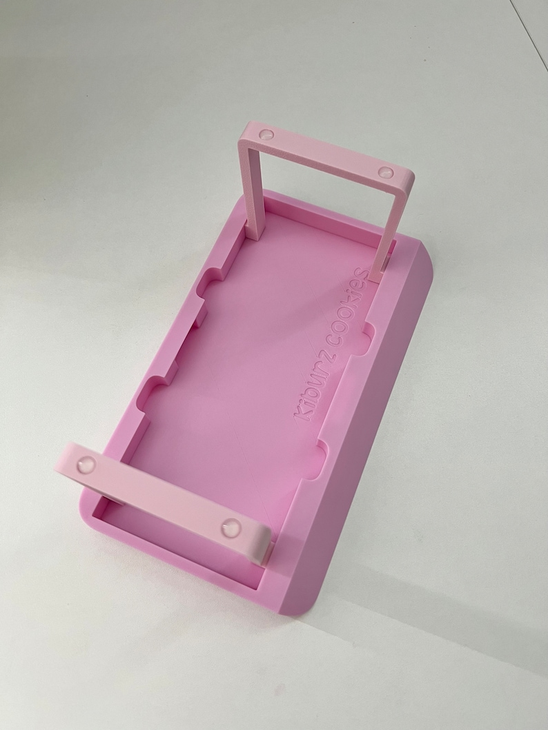May include: Pink plastic cookie tray with two handles and the text "24 Cookies" printed on the front.