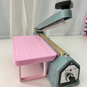 May include: A light blue heat sealer with a pink platform and a control knob labeled "Sealer" and "FS-200".