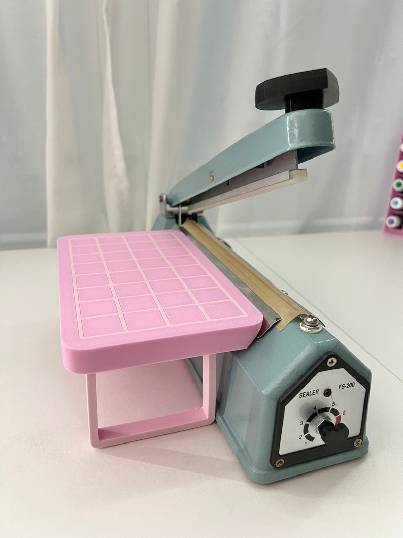 May include: A light blue heat sealer with a pink platform and a control knob labeled "Sealer" and "FS-200".