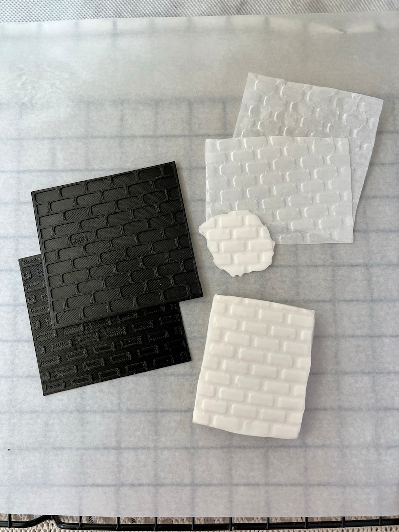 May include: Two sets of brick-patterned embossing tools, one black and one white. The tools are made of a flexible material and are used to create textured designs in fondant or other edible materials.