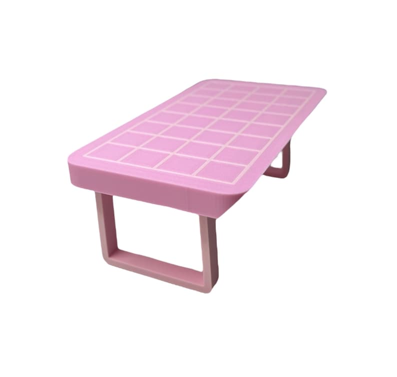 May include: A pink plastic table with a grid pattern on the top and two simple legs. The table is designed for small items and is made of lightweight plastic.