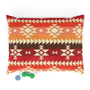 May include: A rectangular pet bed with a red, orange and brown geometric pattern. The bed is filled with a soft, comfortable material. The bed is shown with a blue ball and a green dumbbell toy.