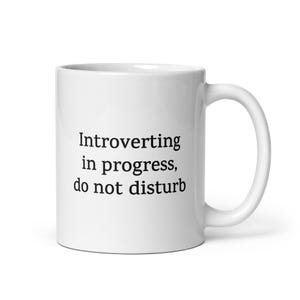 May include: White ceramic coffee mug with black text that reads "Introverting in progress, do not disturb".