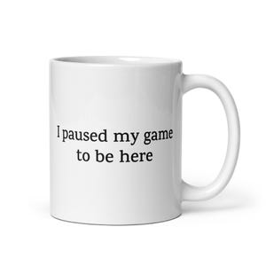 May include: White ceramic coffee mug with black text that reads "I paused my game to be here".