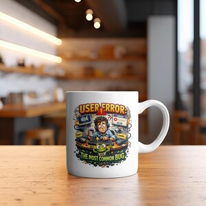 May include: White ceramic mug with a humorous cartoon design. The design features a stressed person at a computer with error messages, the words "USER ERROR" and "THE MOST COMMON BUG". The mug has a curved handle.