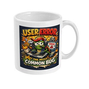 May include: White ceramic mug featuring a colorful cartoon design. The design includes a turtle character wearing headphones and a hat, typing on a keyboard with the text "USER ERROR" and "THE MOST COMMON BUG".