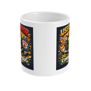 May include: White ceramic mug with a colorful cartoon design. The design features a computer user with the words "ERROR" and "BUG" on one side and "USER" and "COMMAND" on the other. The artwork includes flames, a skull, and a computer.