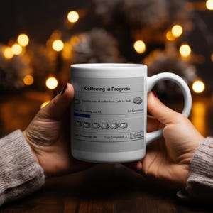 May include: White coffee mug with the text "Coffeeing in Progress" and a graphic resembling a computer progress bar. The mug features a handle and a design that includes coffee cups and a brain icon.