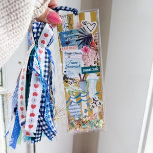 May include: A clear, rectangular bookmark with a tassel. The bookmark features a collage of beach-themed images and text, including "the summer turned pretty" and "Team Jeremiah." The tassel is made of blue, white, and red ribbons.