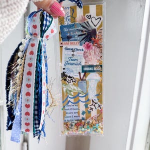 May include: A decorative bookmark with a tassel. The bookmark features a collage of beach-themed images, including seashells, a turtle, and the text "the summer turned pretty". The tassel includes blue, white, and red ribbons.
