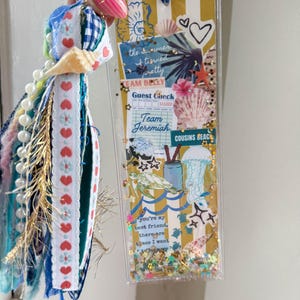 May include: A handmade bookmark with a beach theme. The bookmark features a clear plastic case filled with glitter and decorative elements. The design includes seashells, a turtle, and the text "the summer is timed pretty". A blue and white gingham ribbon is attached.
